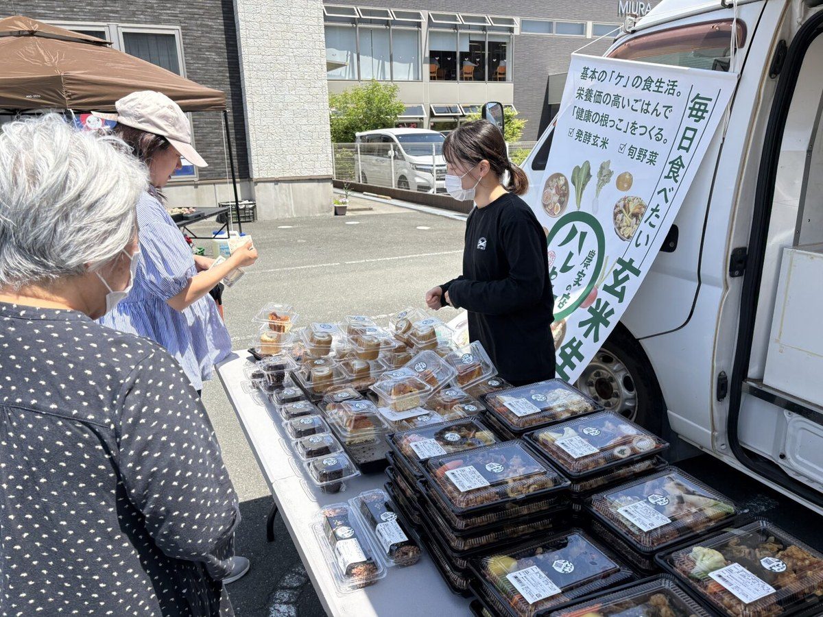 未来マチマルシェの販売テーブルに並ぶお弁当を選ぶ来場者とスタッフ