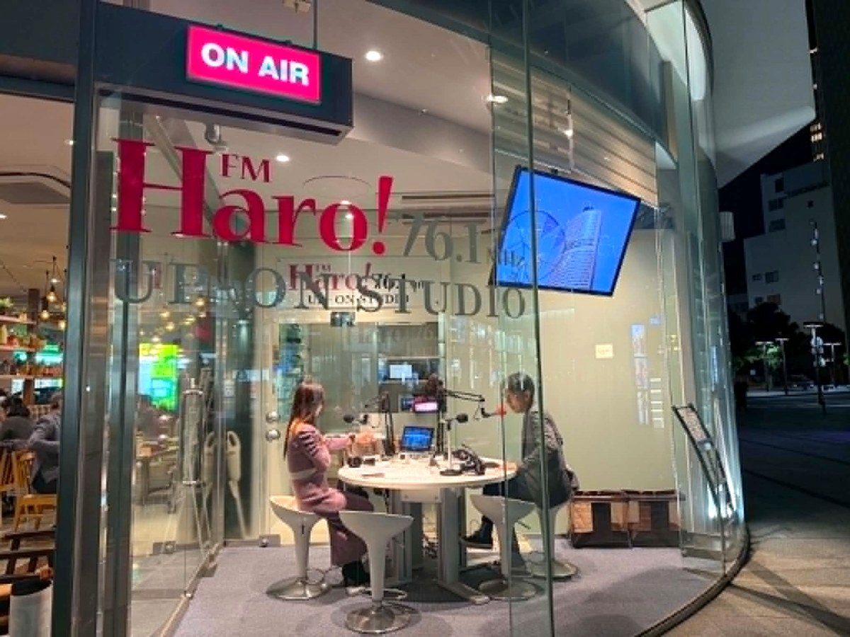 ON AIRの灯りがともるFM Haro!のガラス張りスタジオで収録するパーソナリティと出演者
