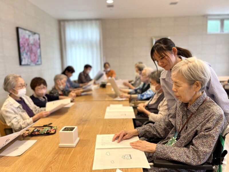 スタッフに見守られながら台本を読む朗読クラブの参加者