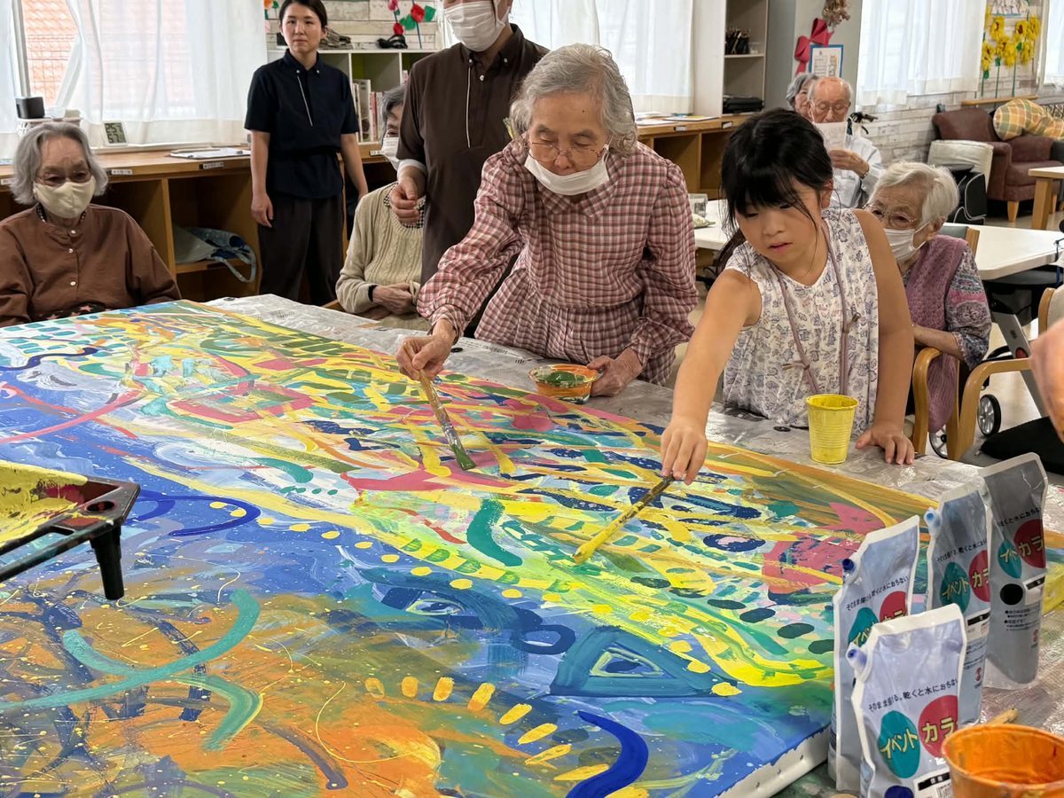 大きな布に色とりどりの絵を描く子どもと利用者